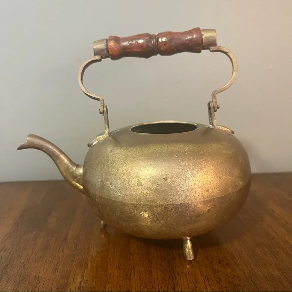 antique brass kettle with a wooden handle and three-legged base.